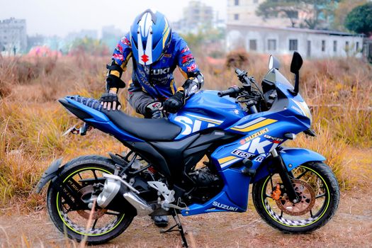 Motorcyclist wearing helmet and gear on a blue Suzuki Gixxer SF sports bike in an outdoor setting.