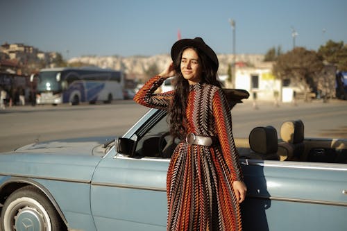 A Woman with a Hat Posing Near a Blue Car