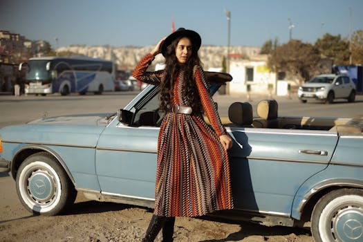 Stylish woman in a long dress poses with a vintage convertible on a sunny day.