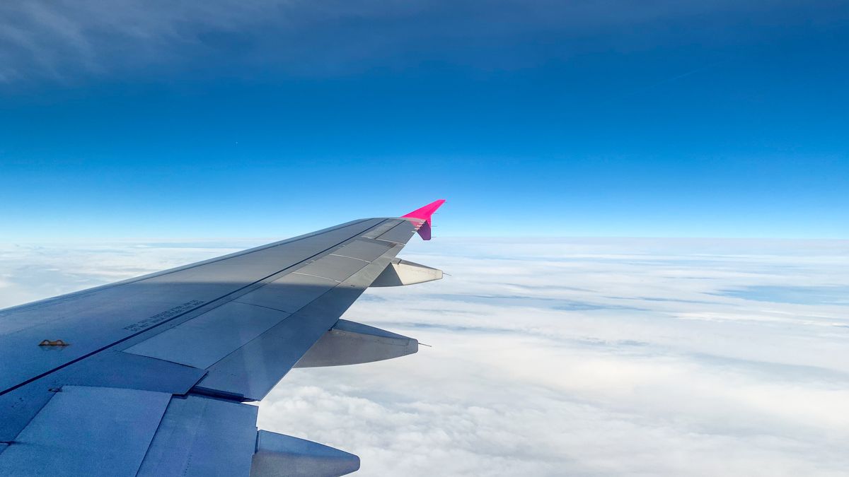 Aerial view of an airplane wing above clouds with clear blue sky, offering serene travel vibes.