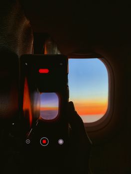 A smartphone records a colorful sunset through an airplane window, creating a vibrant scene.