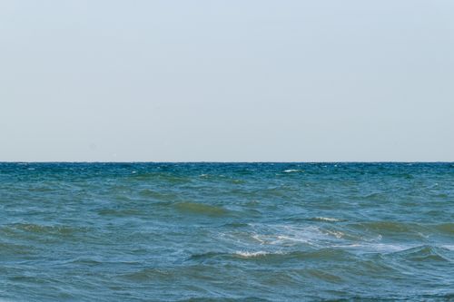 Free Calm ocean waves under a bright blue sky, perfect for relaxation or meditation backgrounds. Stock Photo