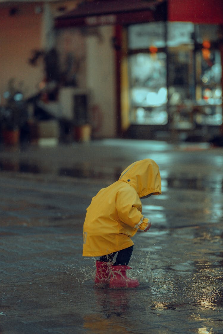 Child In Raincoat Jumping In Puddle