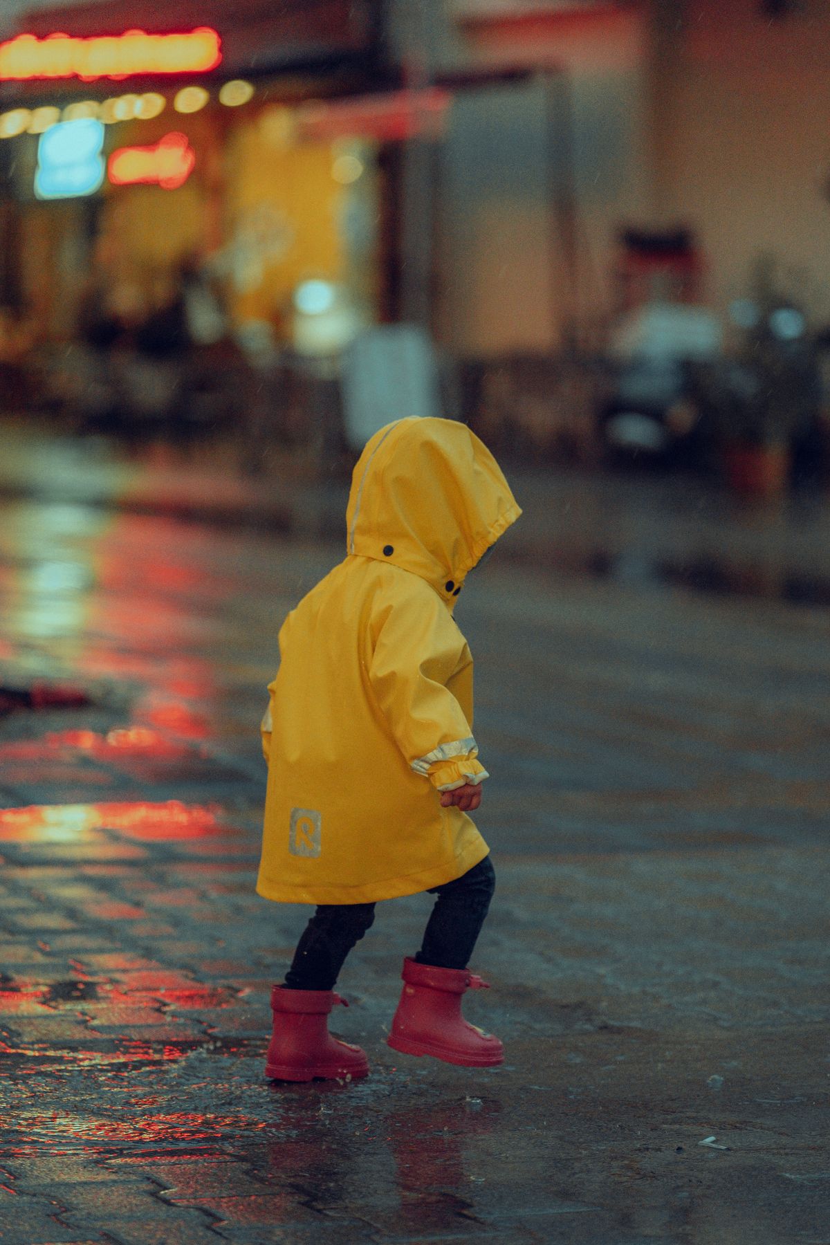 A kid in a yellow raincoat playing in a puddle at night, illustrative of fleece-lined and PU rain gear