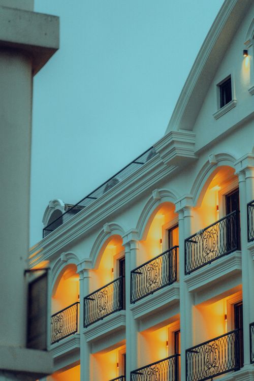 Free Low-angle view of a modern white building with balconies and warm lighting against a blue sky. Stock Photo