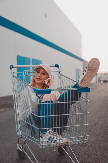 Playful portrait of a young woman enjoying a sunny day, sitting inside a shopping cart.