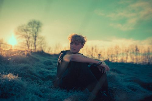 Free A young man sits in a frosty meadow at sunrise, capturing a serene and contemplative moment. Stock Photo