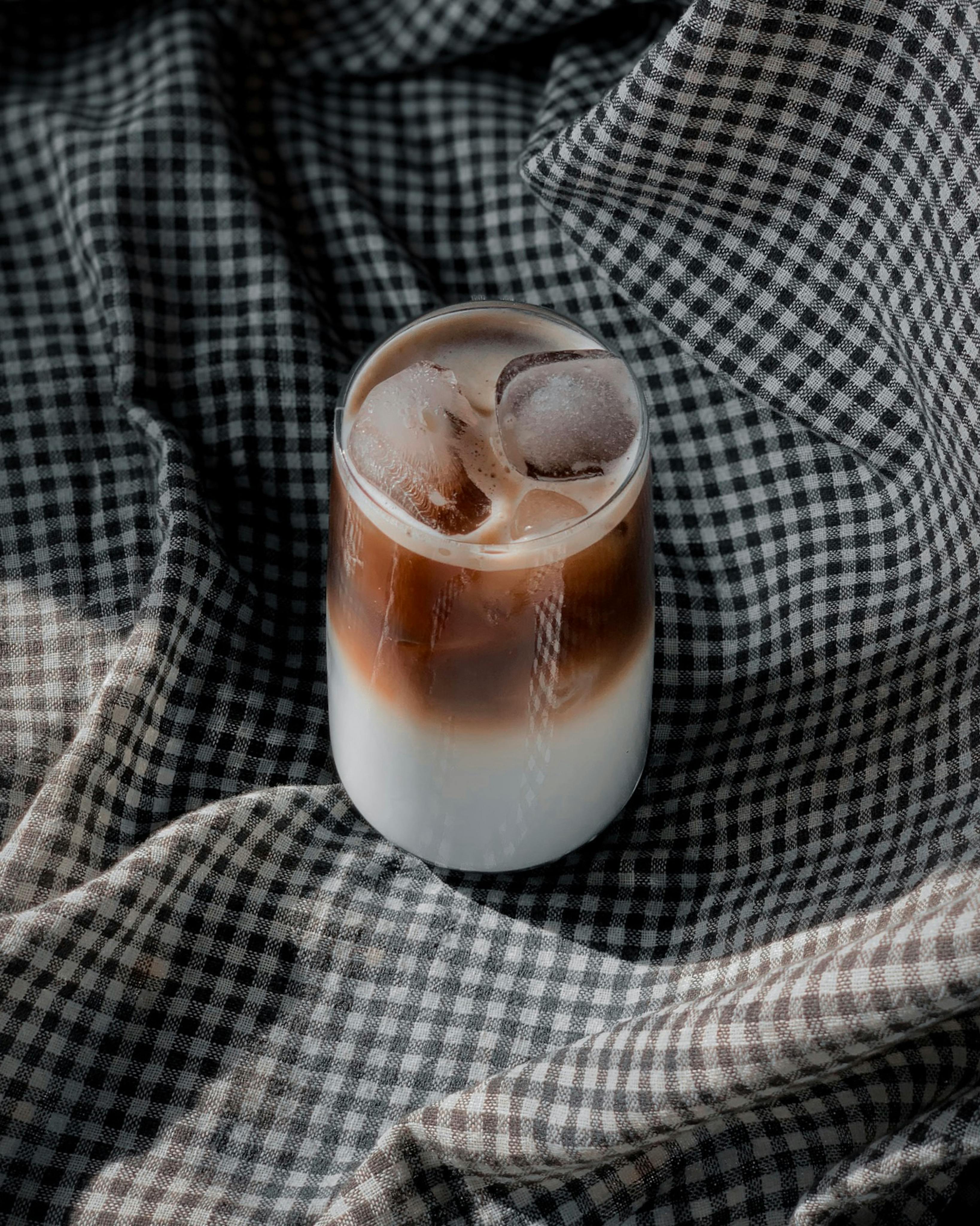 A delicious iced coffee with ice cubes on a black and white checkered background.
