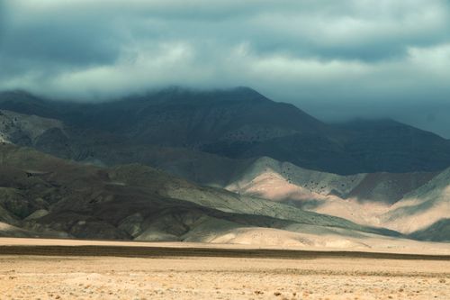 Free Calming image of desert hills with a moody, cloudy sky, casting shadows over rock formations. Stock Photo