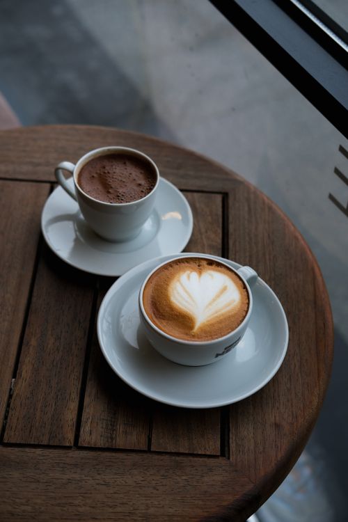 Free Two artistic coffee cups with latte art on round wooden table indoors. Stock Photo
