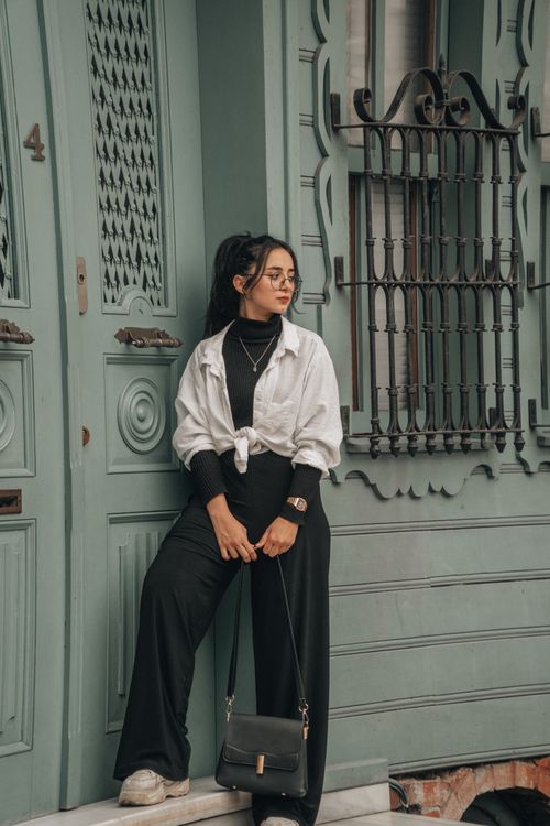 Free Stylish woman in black pants and white jacket standing by an ornate door, exuding sophistication. Stock Photo