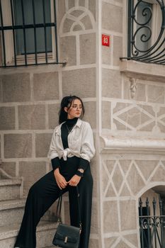 A fashionable woman with glasses and a chic outfit leaning against an ornate building facade.