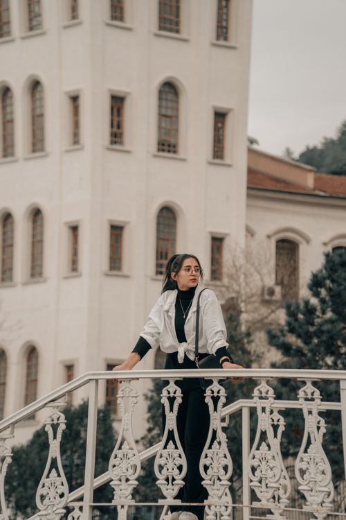 Free Stylish woman standing on an intricately designed iron bridge in a city setting, exuding modern elegance. Stock Photo
