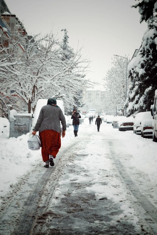 Free A picturesque winter scene in Malatya showing a snowy street with pedestrians and parked cars. Stock Photo