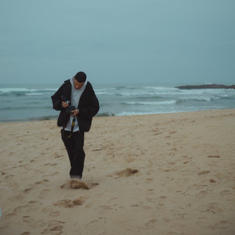 Photo Of A Man Walking On The Beach And Keeping Camera In His Hand