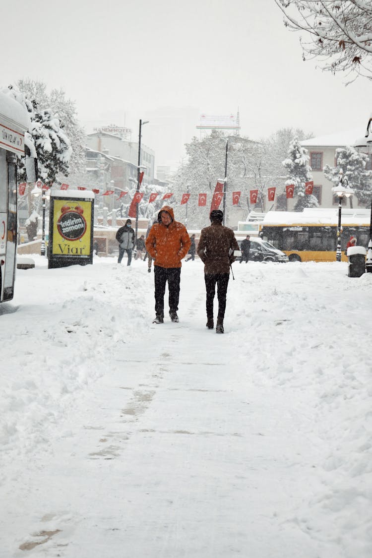 A Group Of People Walking On A Snow Covered Ground Near Cars