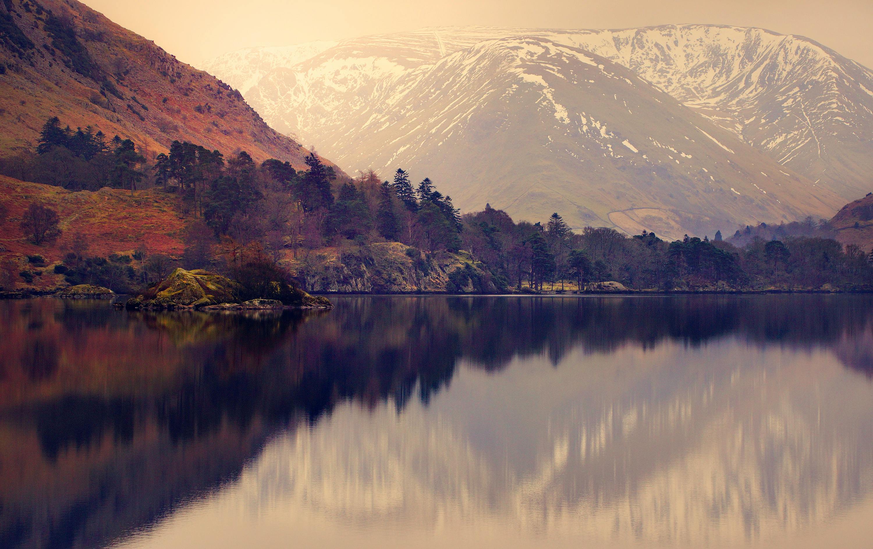 白雪皑皑的山峰和树木倒映在宁静的山间湖泊中，构成一幅宁静的自然景观