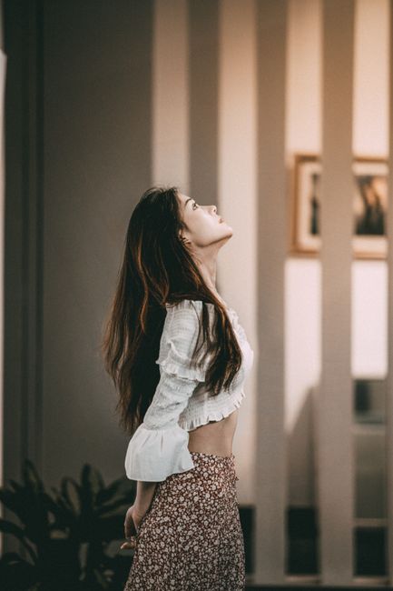 Artistic side profile shot of a woman indoors with long brown hair, wearing a ruffled blouse and floral skirt.
