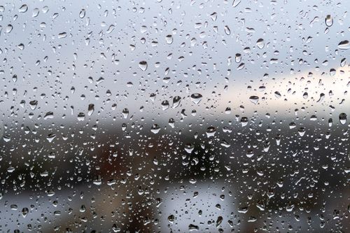 Free A close-up view of raindrops on window glass with a blurred landscape in the background. Stock Photo