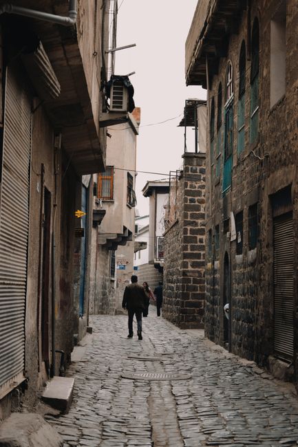 Fotomural Una figura solitaria camina por un callejón de adoquines flanqueado por edificios históricos de piedra.