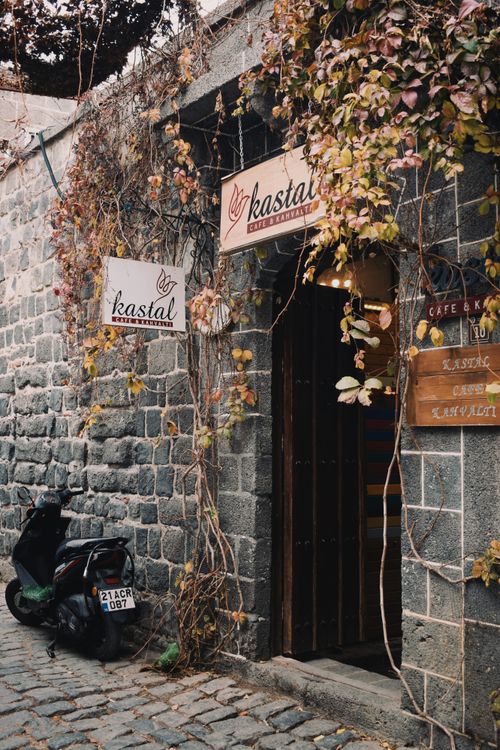 Free Rustic café entrance with climbing vines on stone wall and parked motorcycle, creating a cozy street scene. Stock Photo