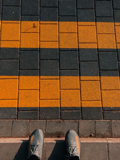 Free A vibrant urban scene featuring distinct yellow road markings on tiled pavement with shoes visible in the foreground. Stock Photo