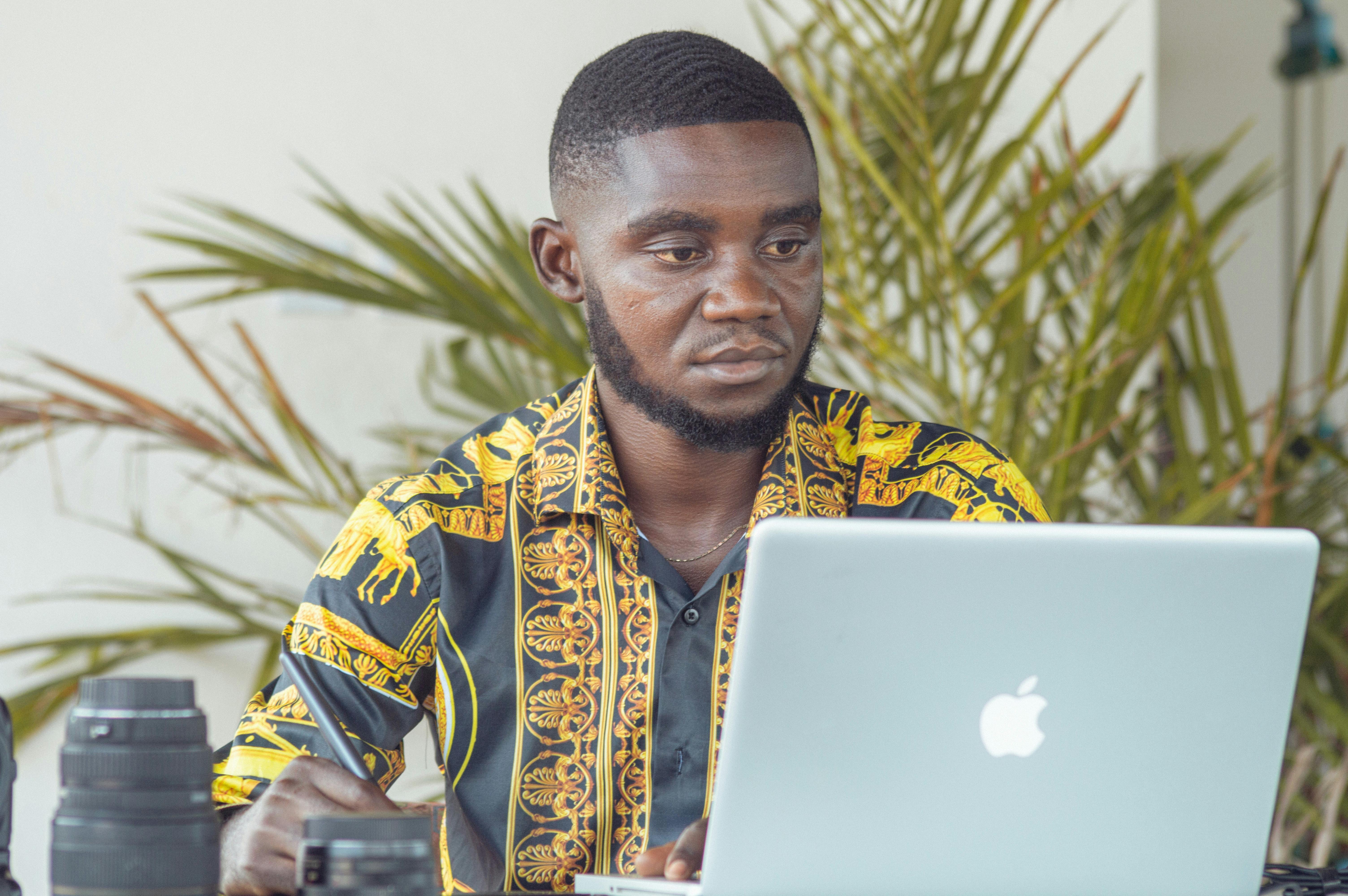 African man using a laptop outdoors with camera equipment in Douala, Cameroon.