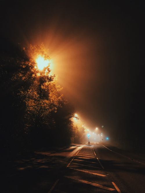 Free Eerie night view of a misty London road illuminated by foggy street lamps casting mysterious light beams. Stock Photo