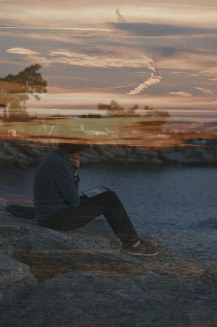 Dreamlike double exposure of a person at the seaside with a vibrant sunset reflection, invoking imagination.