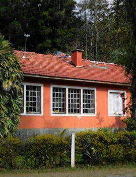 Charming bungalow with red roof surrounded by lush greenery and vibrant plants.