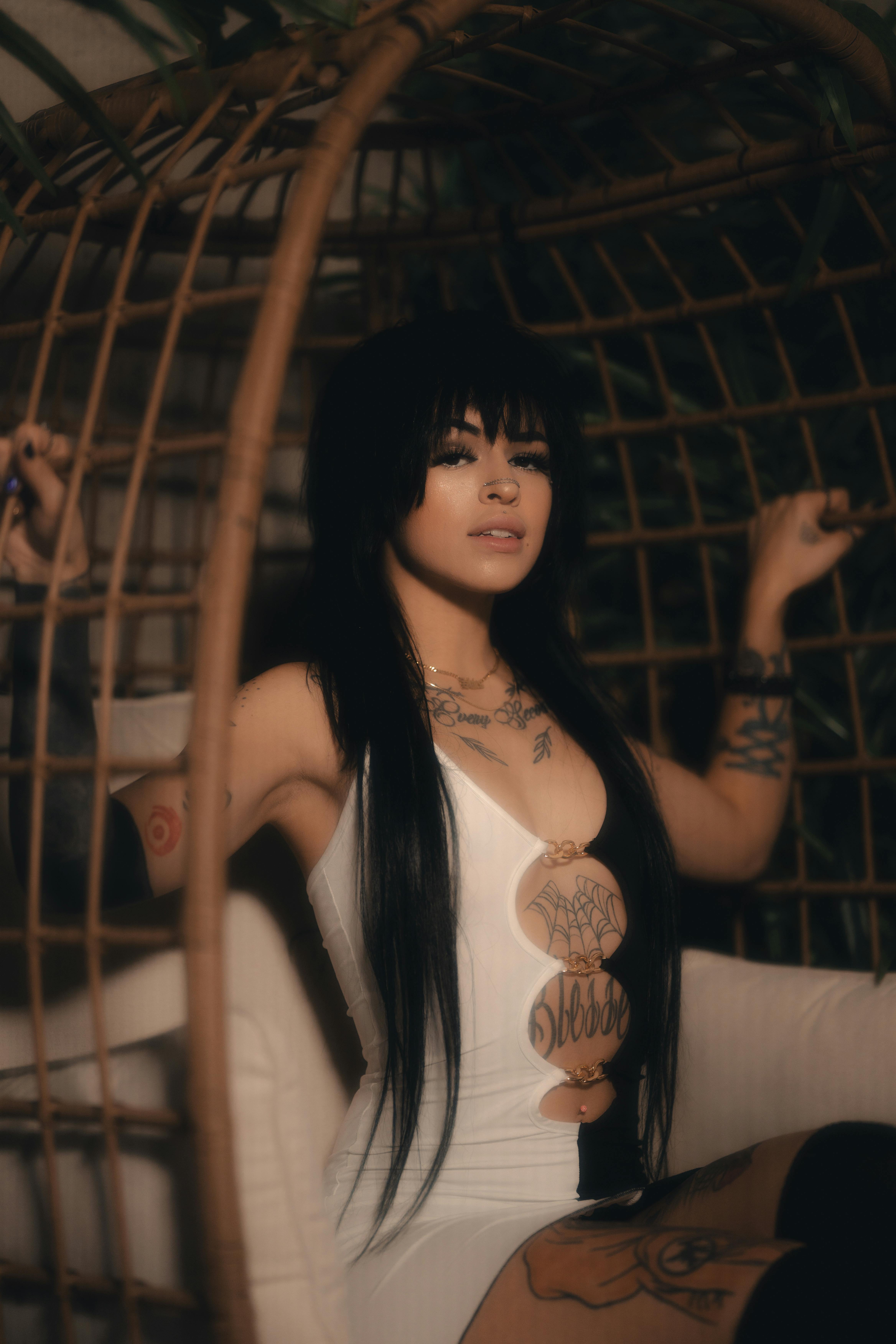 Fashionable woman with tattoos sits confidently in a wicker chair, exuding modern style and elegance.