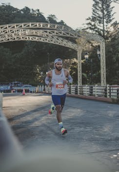 Athlete running marathon on a sunny day under decorative bridge, showcasing endurance and sportswear.