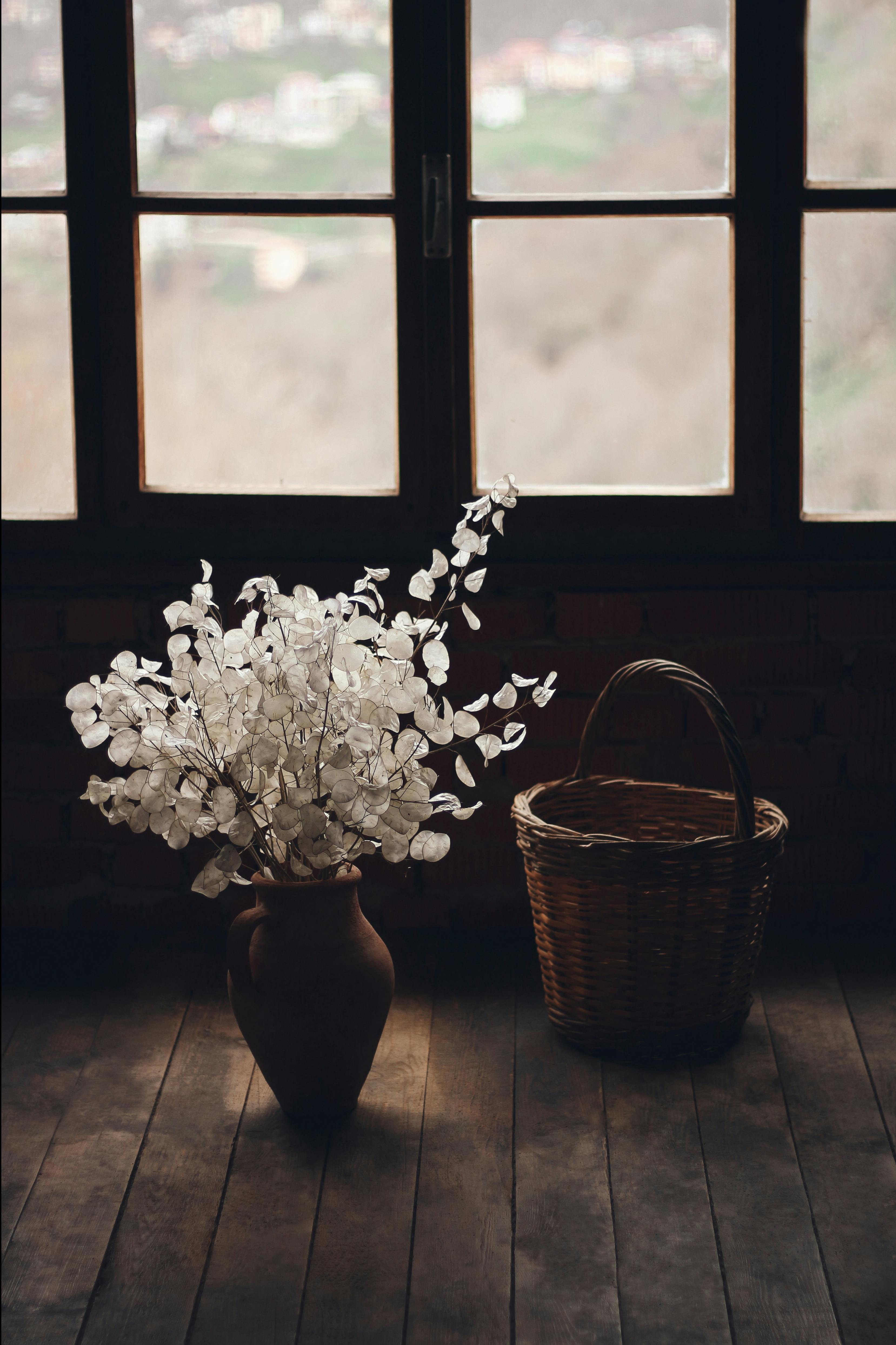 A cozy rustic interior featuring a vase with flowers and a wicker basket by an old window.