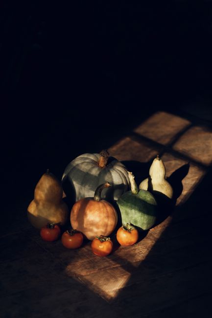 Warm, dramatic still life featuring autumn squash and ripe persimmons in artistic shadows.