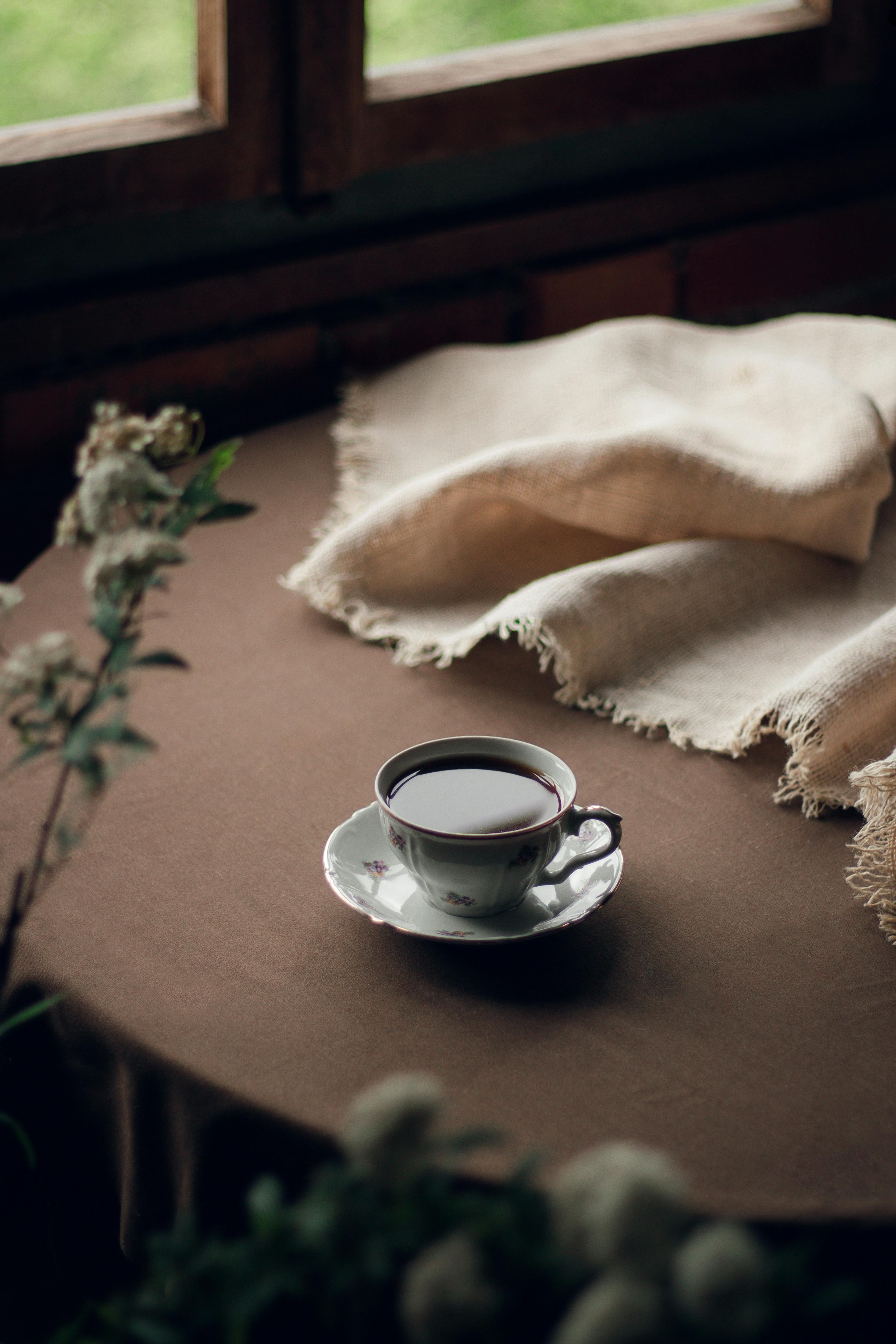 Elegant coffee cup on rustic table with warm fabric, softly lit ambiance.
