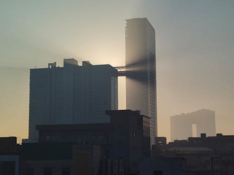 Dramatic sunrise over Noida's skyline with sun rays peeking through modern skyscrapers.