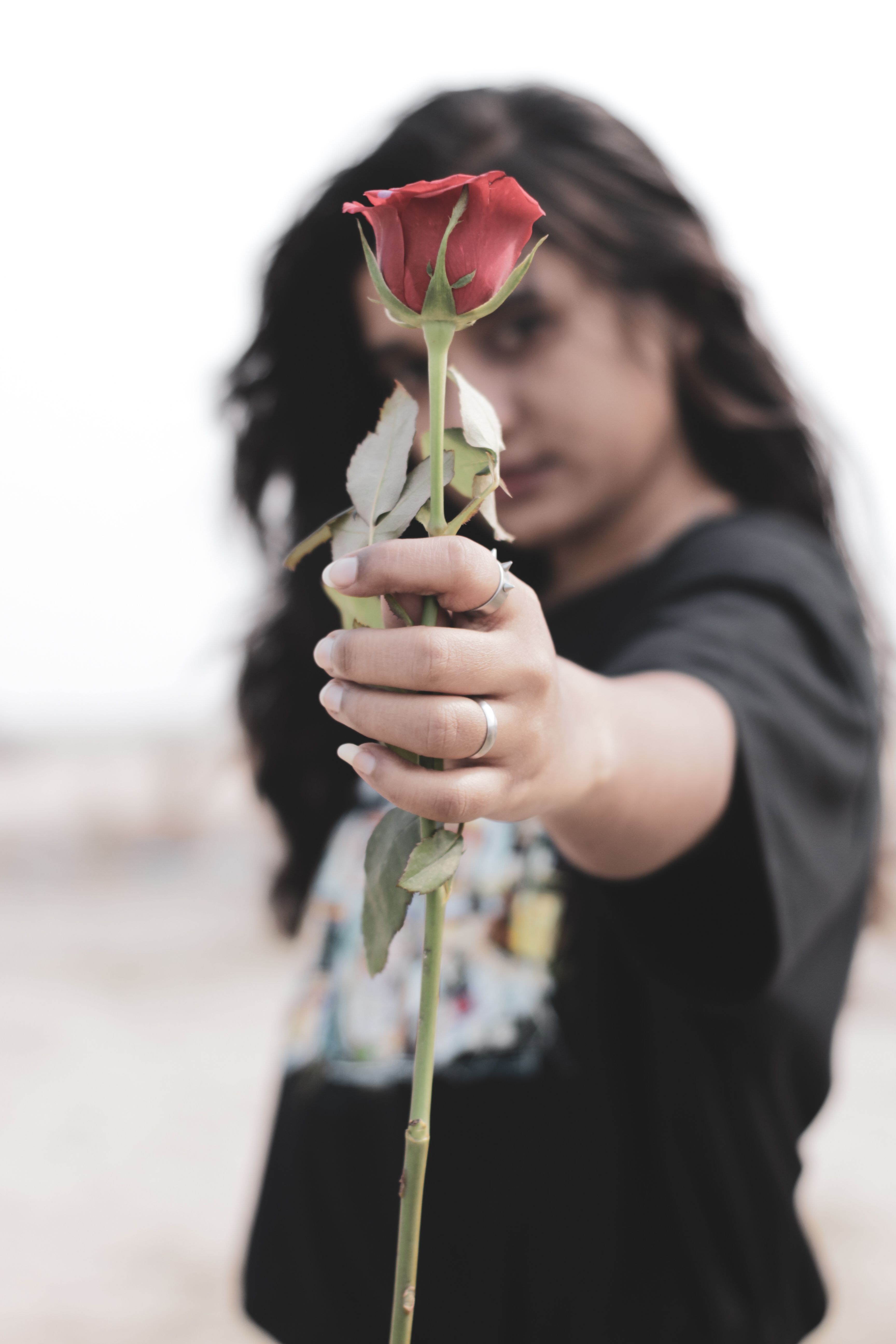 Young woman in focus holding a vibrant red rose with a blurred background for artistic depth.