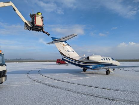 A private jet undergoing de-icing on a snow-covered airport tarmac in winter weather.