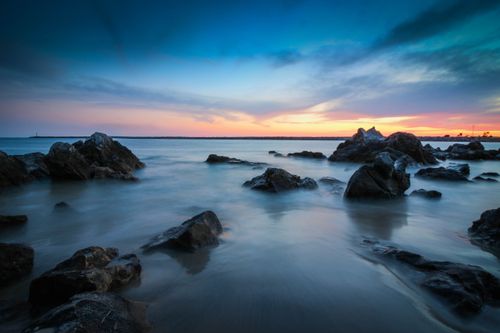 Free Serene sunset over rocky seashore at Tustin Beach, showcasing vibrant colors and gentle waves. Stock Photo