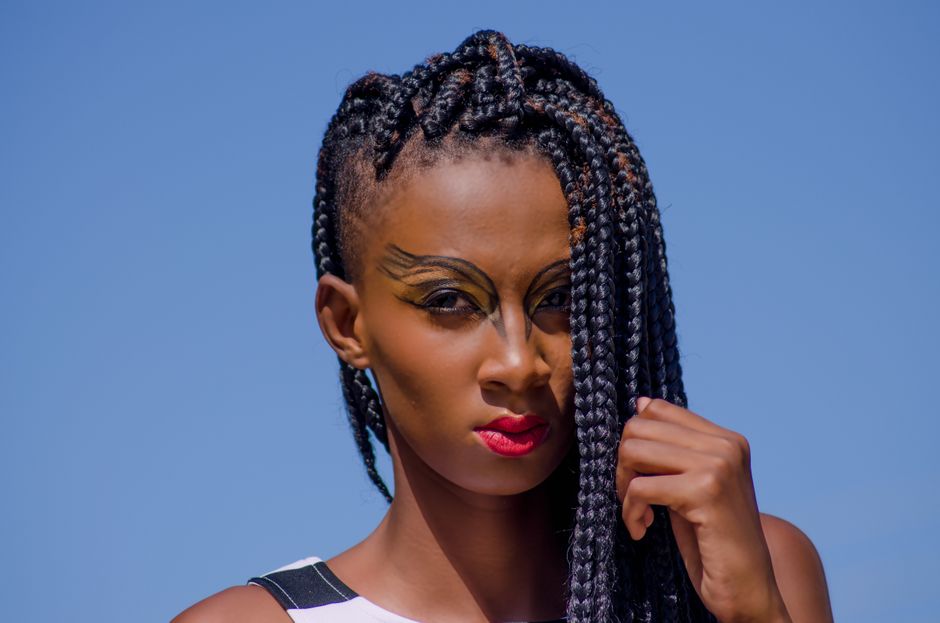 Striking portrait of a woman with bold makeup and intricate braids, set against a clear blue sky.