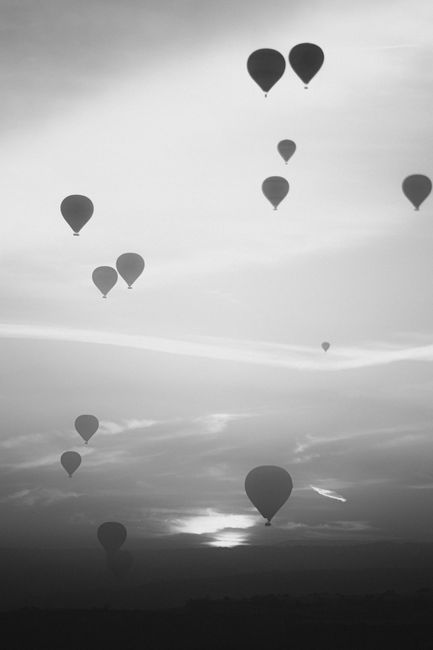 Captivating grayscale image of hot air balloons floating in the sky at twilight, showcasing their serene ascent.