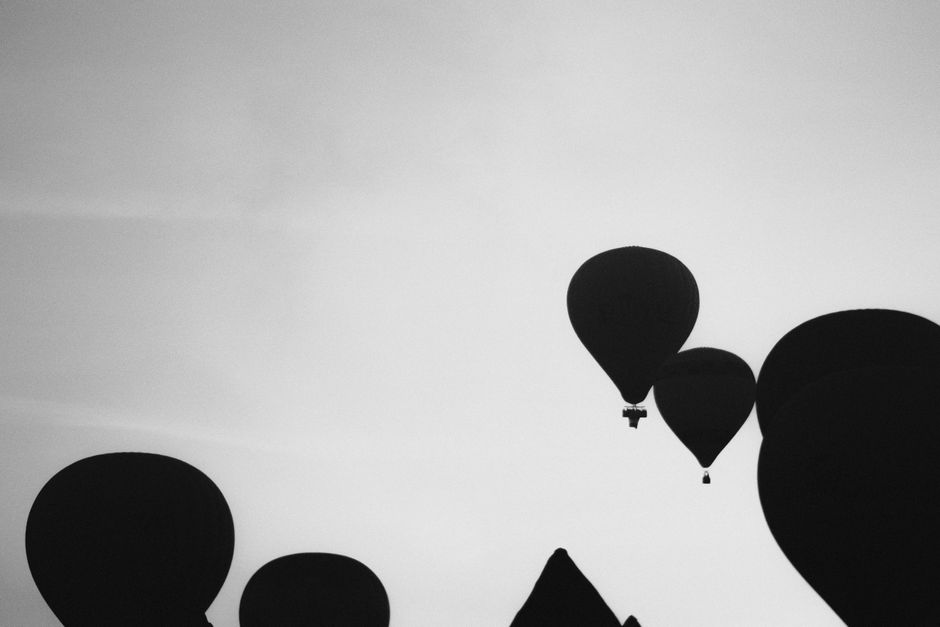 Monochrome silhouette of hot air balloons floating against a clear sky.