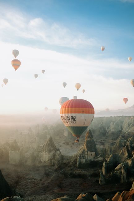 Stunning view of hot air balloons floating above Cappadocia's unique rock formations at sunrise.