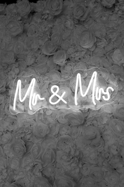 Black and White Photo of an Illuminated Sign on the Background of Flowers at a Wedding 