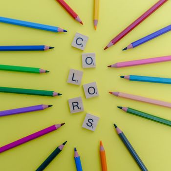 Arrangement of multicolored pencils and Scrabble letters on a yellow background.（イメージ）