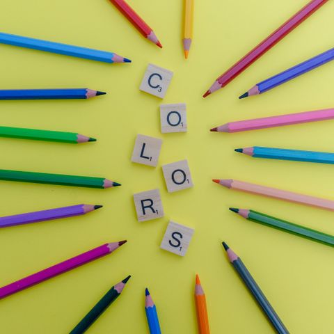 Coloured pencils fanned around lettered tiles on a yellow ground. Photo by Patricia Luquet on Pexels