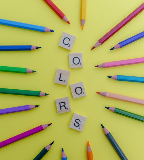 Top View of Multicoloured Pencils and Wooden Letters on a Yellow Background