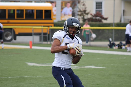 A young football player catches a pass during a game, wearing full uniform and helmet.