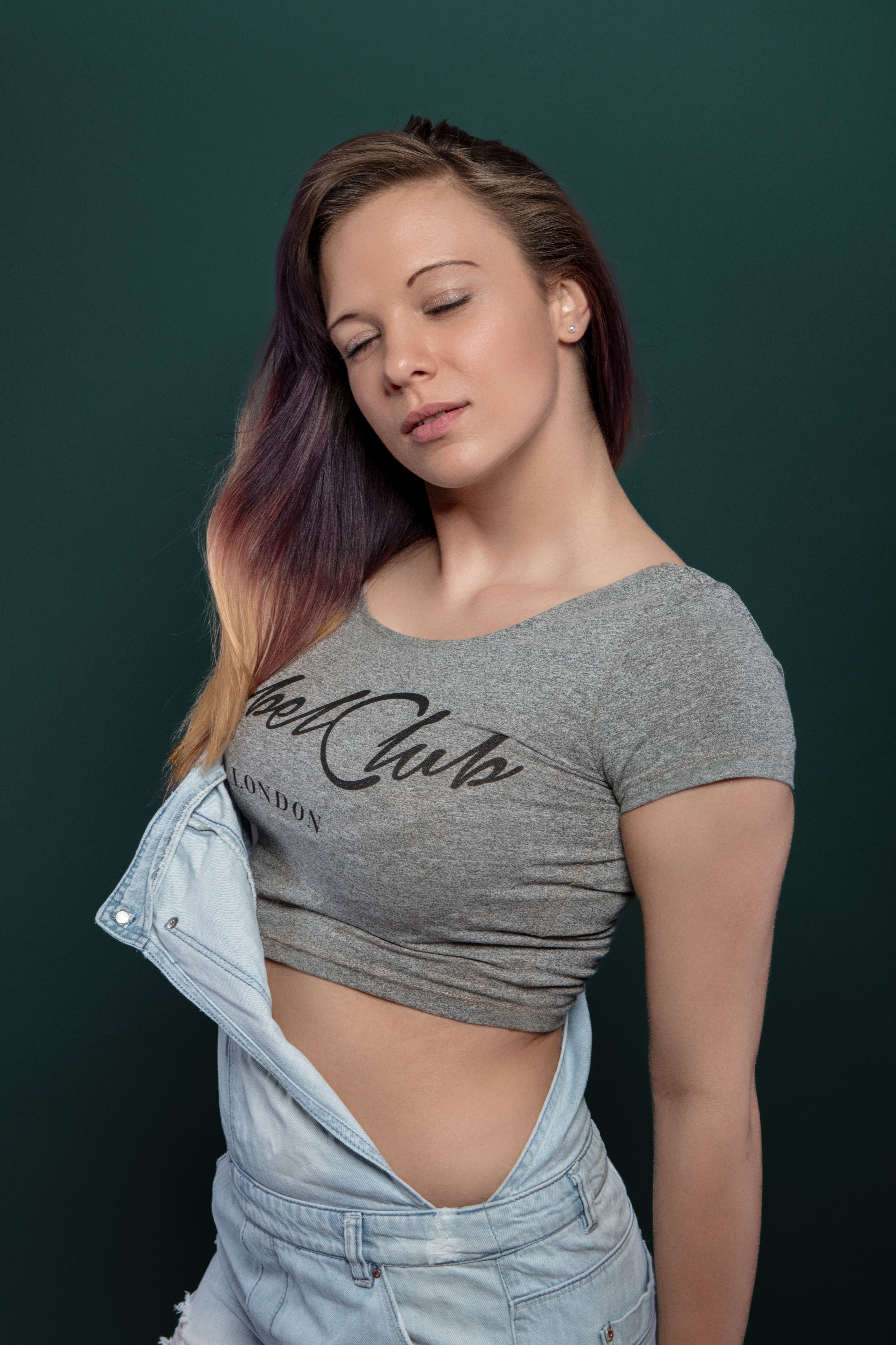 Stylish model posing with dyed hair and gray crop top against a green backdrop in studio.