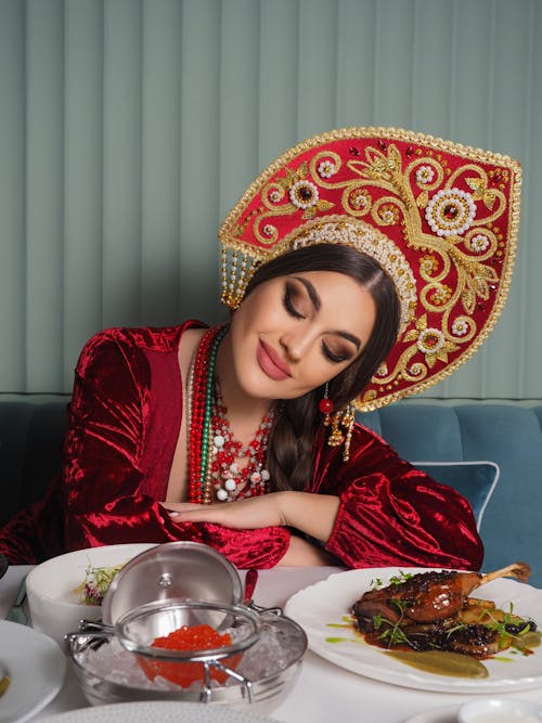 Woman Wearing Ornamental Hat and Red Dress Looking at a Table with Food